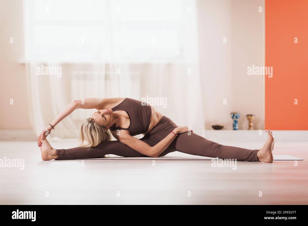 A woman in sportswear practicing yoga performs an exercise with head turning to her knees, Parivritta Janu Shirshasana, exercising in the studio while Stock Photo