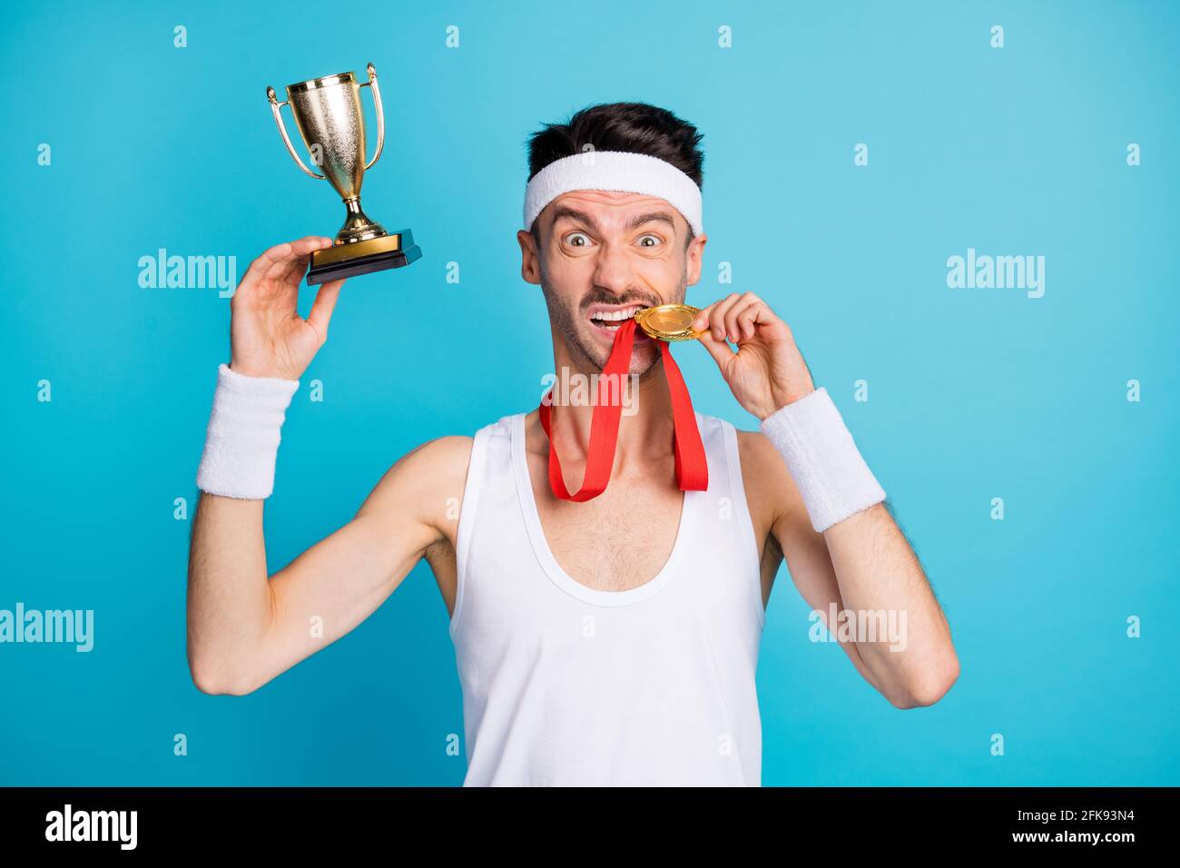 Photo of brown haired lucky man win medal golden trophy bite teeth isolated on blue color background Stock Photo