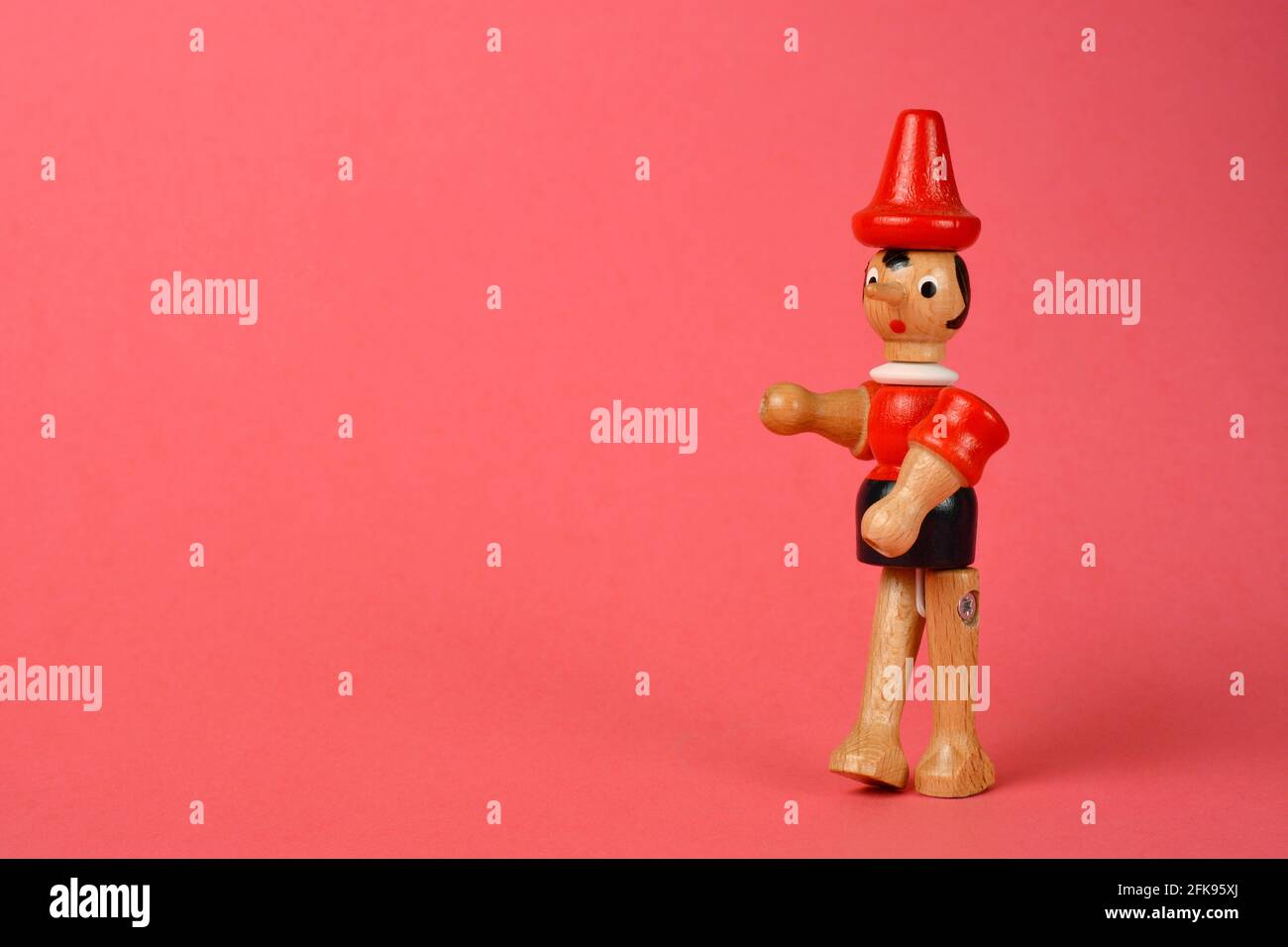 Wooden puppet depicting Pinocchio walking on a pink background Stock Photo