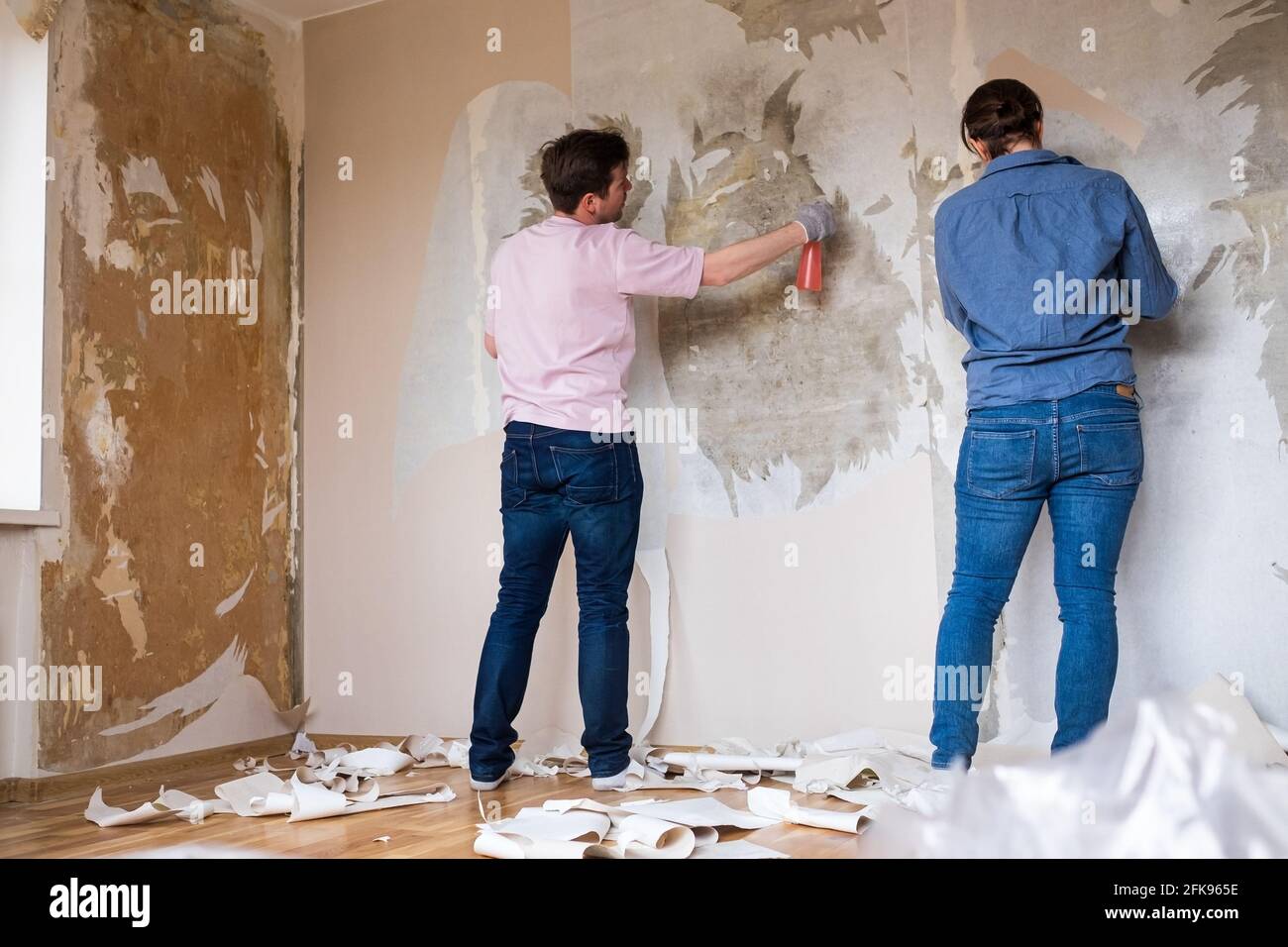 Young caucasian couple removing old wallpaper from walls preparing for