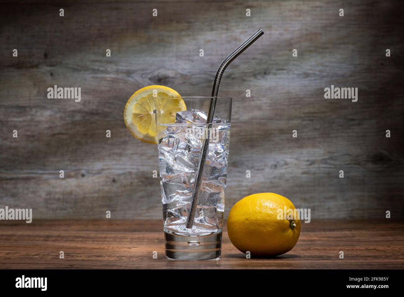 Glass of water with ice and lemon and a stainless steel straw in a highball glass. Stock Photo