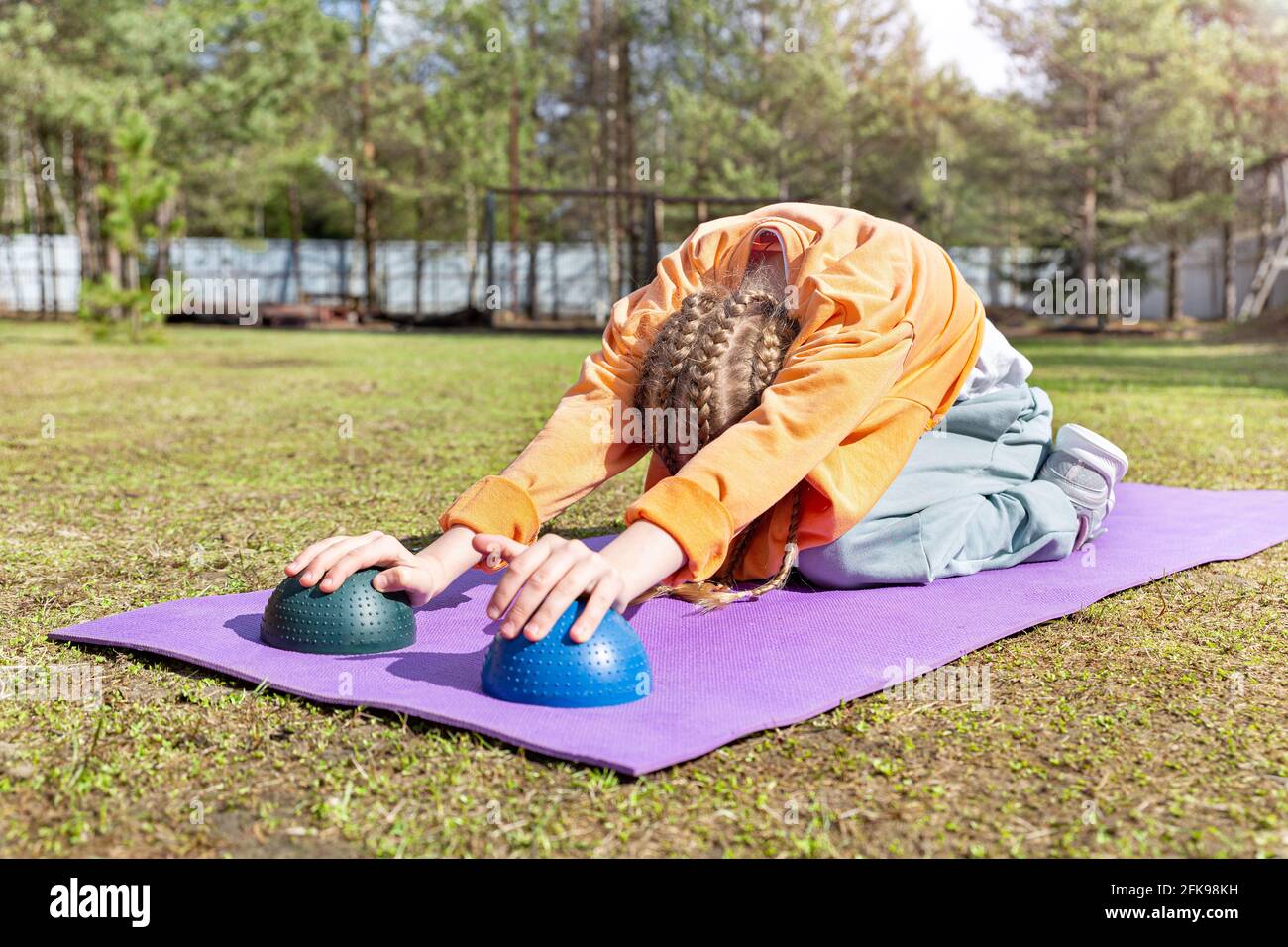 The girl goes does stretching on a sports mat on a summer sunny day. Stock Photo