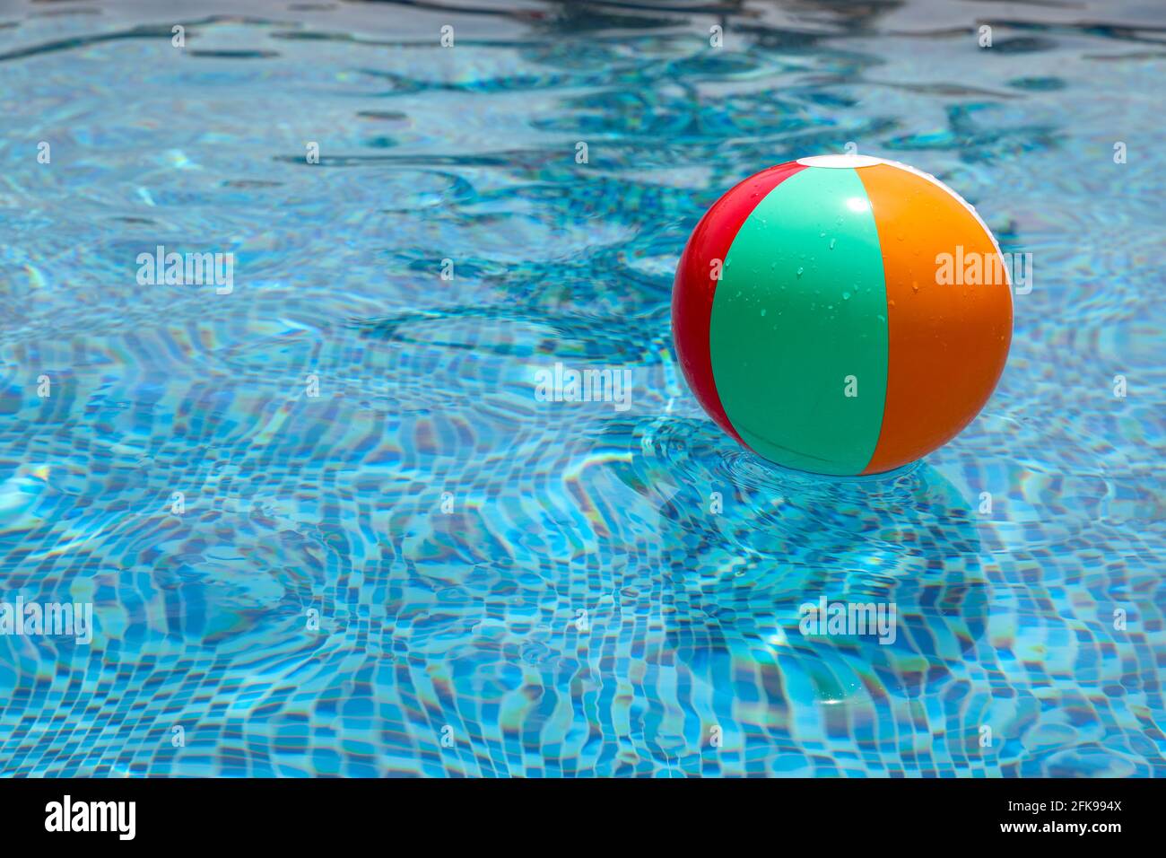 Beach ball in pool. Colorful inflatable ball floating in swimming pool, summer vacation concept. Stock Photo