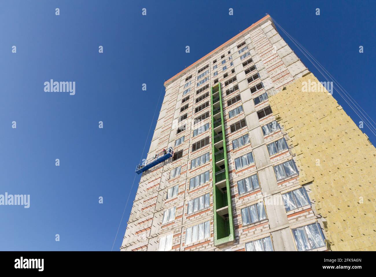 Construction suspended cradle. Construction cradle with workers on the facade of the building. Insulation of building walls with insulation. Stock Photo