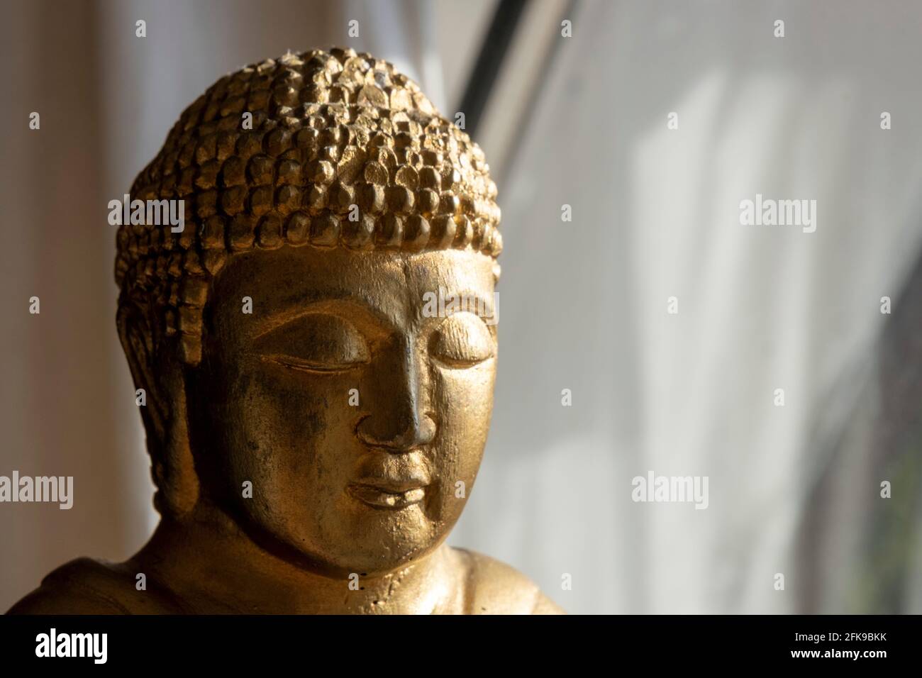 Buddhism and meditation concept: Close up on the head of a golden Buddha statue with copy space. Zen-like spirituality. Religious sculpture. Stock Photo