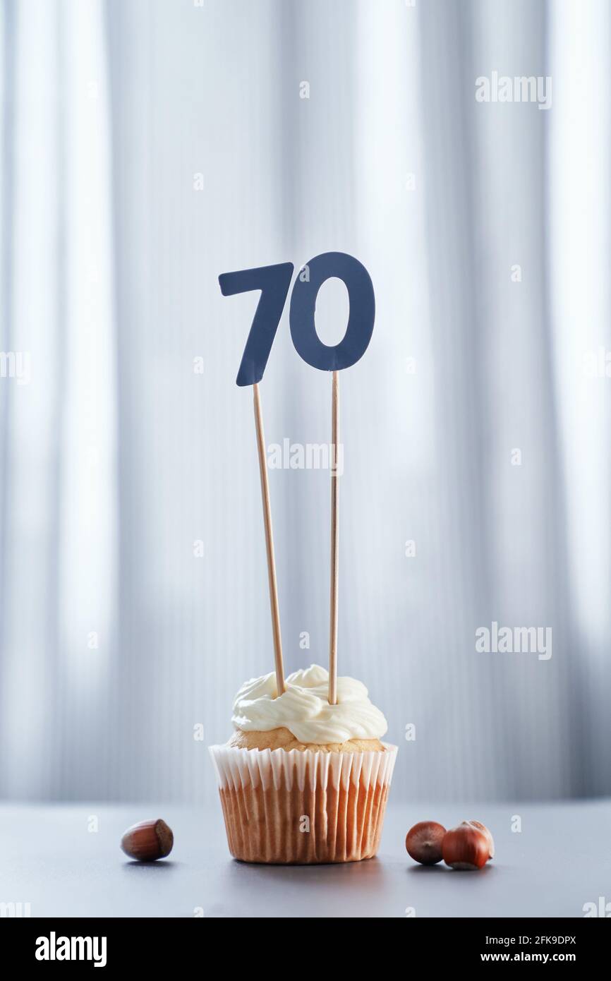 Anniversary greeting card concept. Tasty vanilla cupcake or muffin with number 70 seventy and hazelnuts with bright background. Minimalistic birthday cake concept. High quality vertical photo Stock Photo