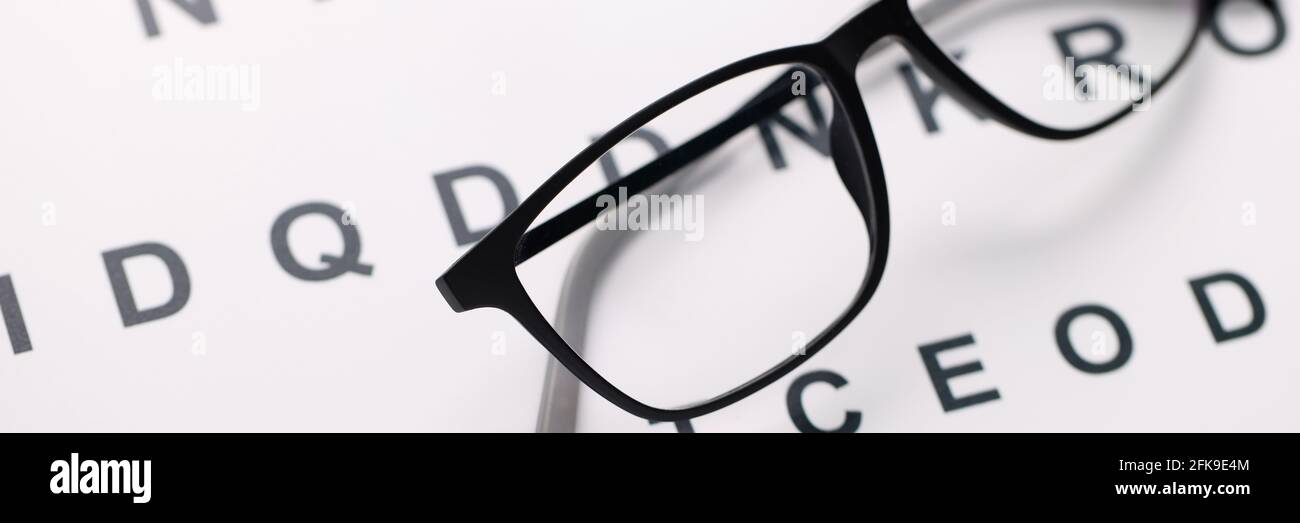Glasses for vision in black frames lying on test chart closeup Stock Photo