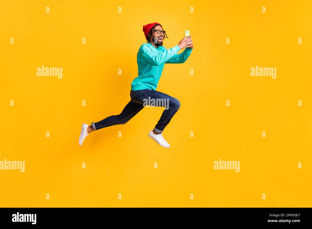 Full size profile photo of brunette optimistic guy jump run take photo wear cap spectacles pullover jeans isolated on yellow background Stock Photo