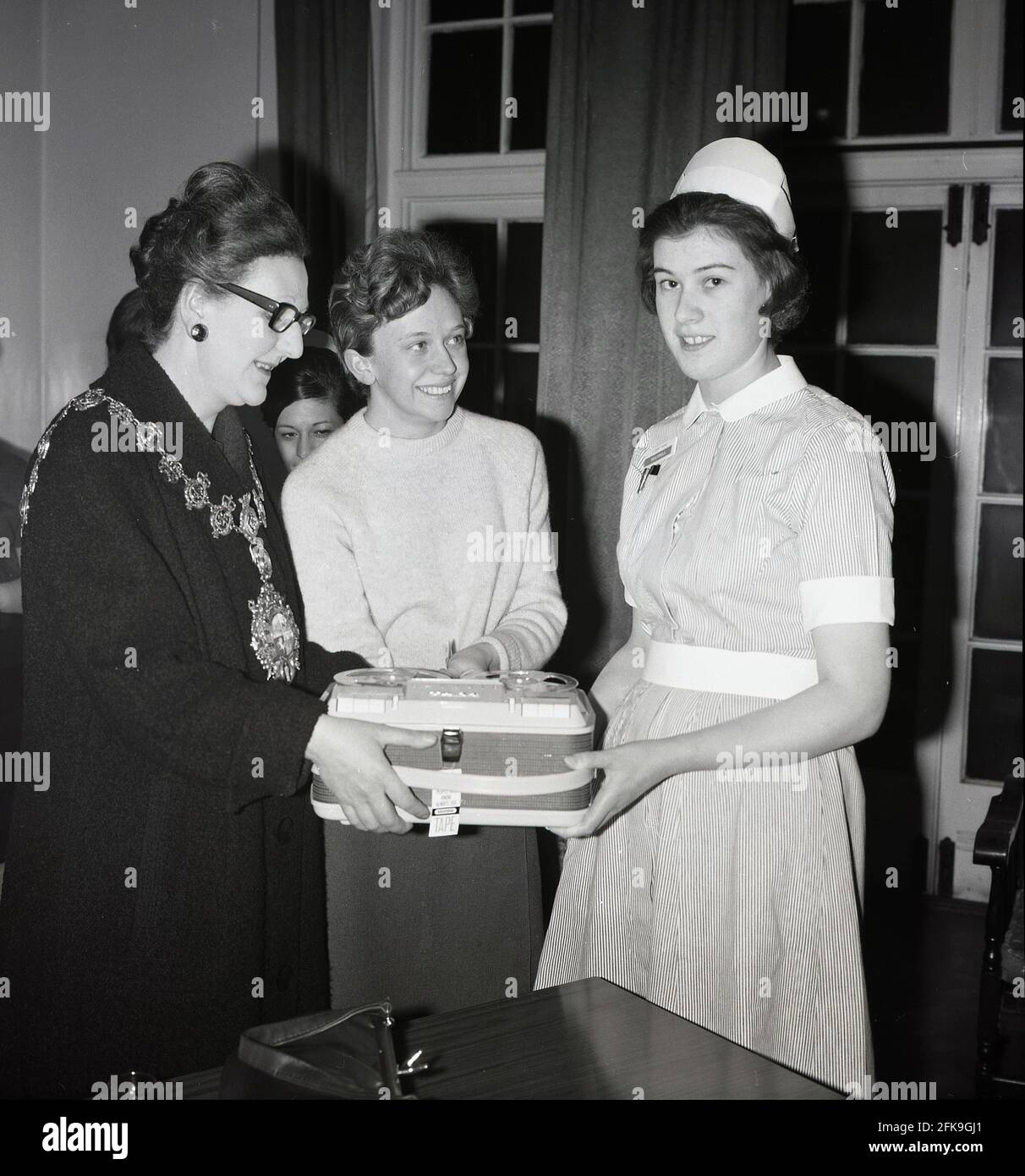 1960s, historical, inside a hospital, a nurse receiving a prize of a portable reel to reel Grundig tape recorder, from the Lady Mayoress, Southeast London, England, UK. Stock Photo