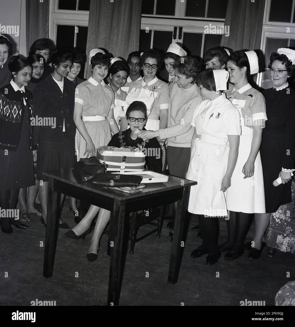 1960s, historical, at a South East London hospital, a group of nurses stand around a seated Lady Mayoress, with one of them recording her speaking using a Grundig portable reel to reel tape recorder. Established in 1945 in Nuremberg, Germany by radio dealer, Max Grundig, the German manufacturer's audio consumer electronic products were highly regarded in this era. Stock Photo