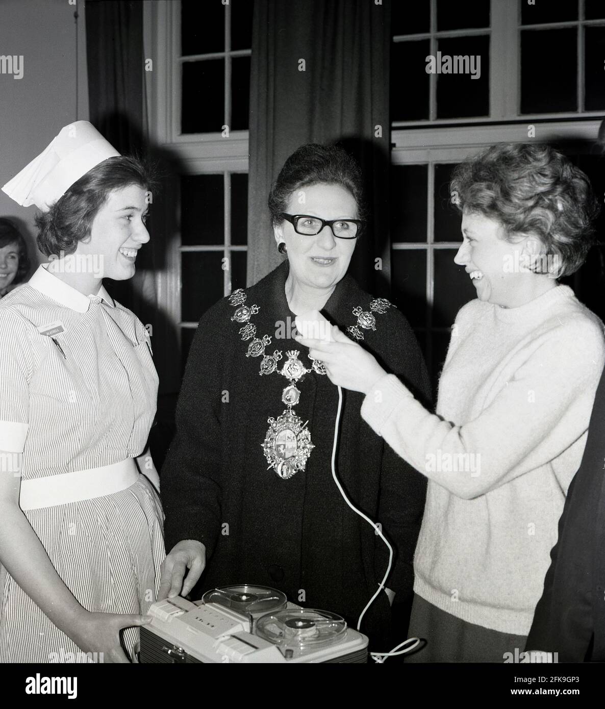 1960s, historical, at a South East London hospital, smiles all round as a nurse and a local female journalist stand beside a Lady Mayoress, recording her speaking with a portable reel to reel tape recorder. Stock Photo