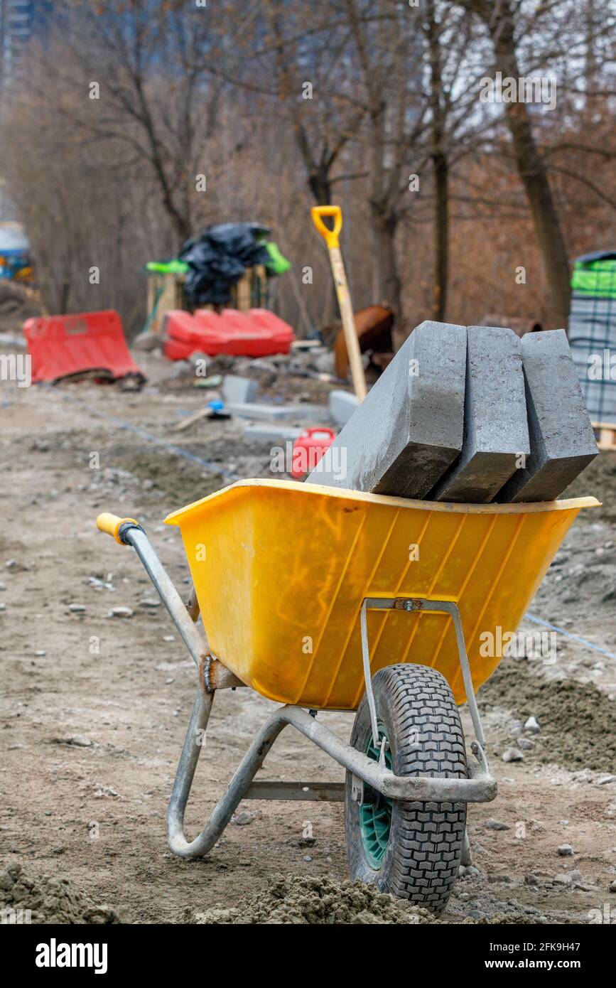 Concrete curb blocks lie inside a construction wheelbarrow against the backdrop of a workplace in blur. Stock Photo