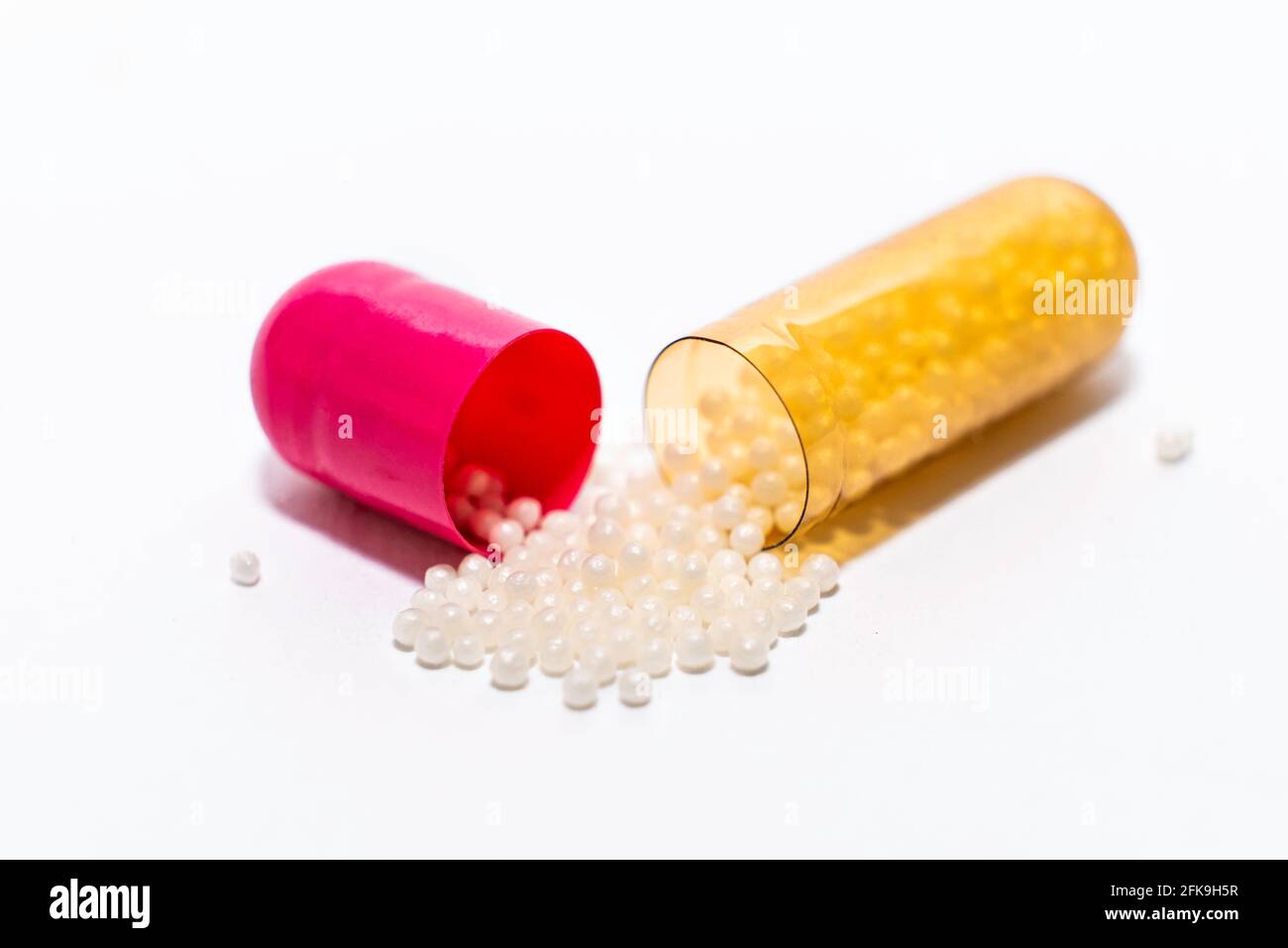 Closeup one opened pink yellow soft capsule pill with powder on white