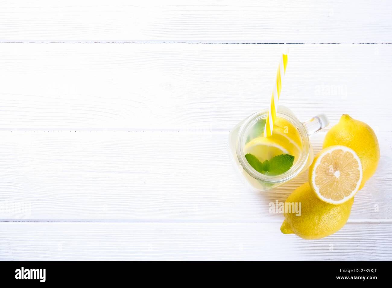 One mason jar glass of homemade refreshing lemonade with slices of organic ripe lemon, whole and halved. Non alcoholic beverage on a rustic white wood Stock Photo