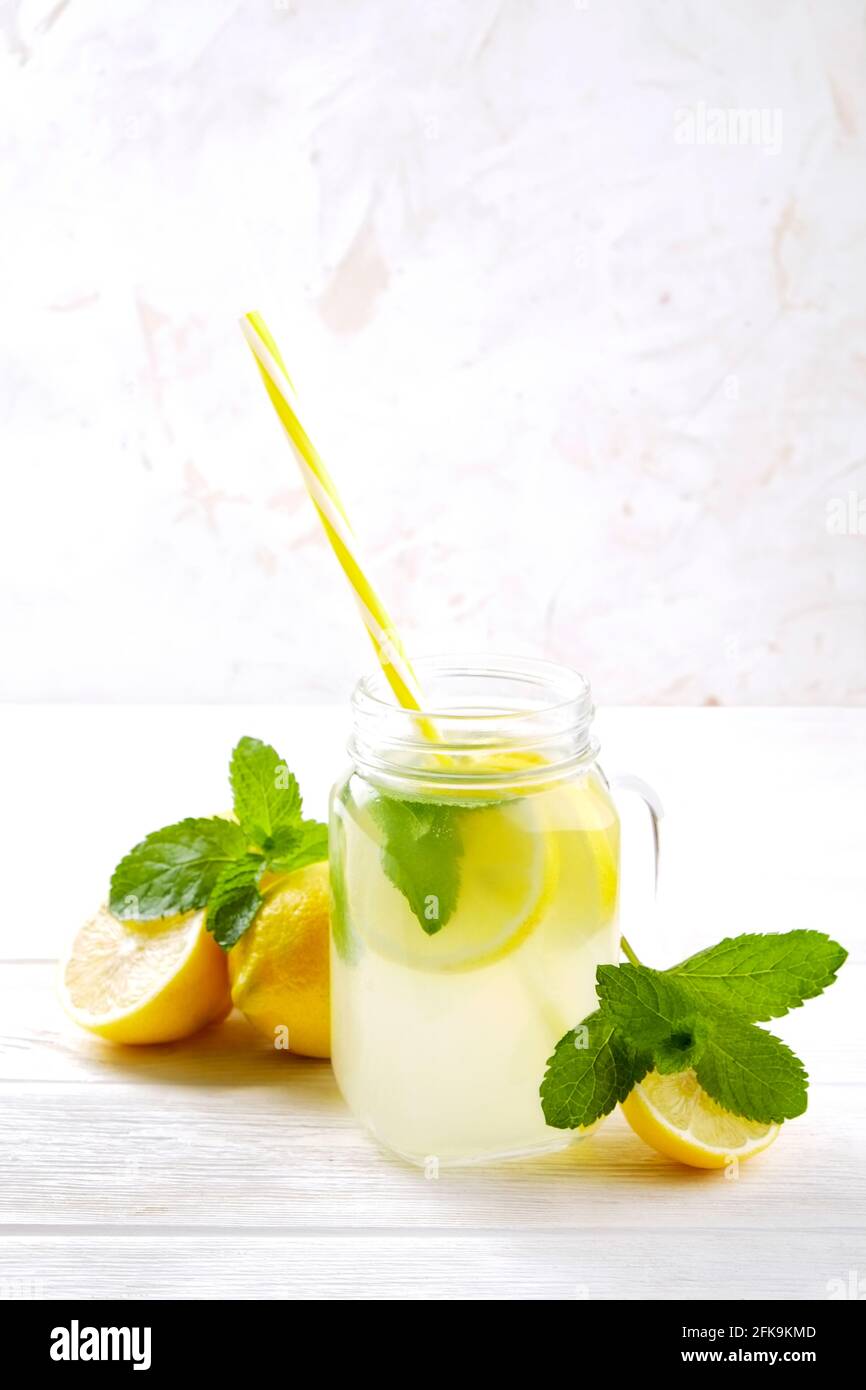One mason jar glass of homemade refreshing lemonade with slices of organic ripe lemon, whole and halved. Non alcoholic beverage on a rustic white wood Stock Photo