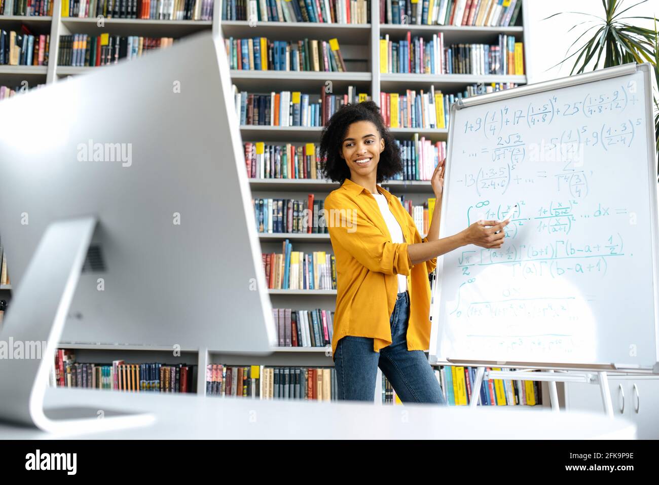 Stylish African American female coach, stands at whiteboard, in casual  clothes, uses computer, leads an online lesson, communicates with students  via video conference, looks at screen,distant learning Stock Photo - Alamy