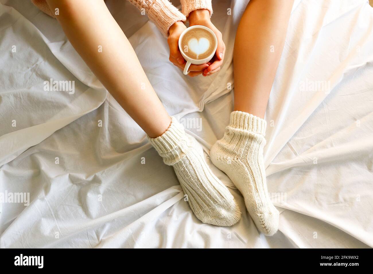 https://c8.alamy.com/comp/2FK9WX2/young-woman-drinking-cappuccino-coffee-and-sitting-in-bed-with-white-linnen-top-view-of-female-legs-in-warm-wool-socks-sweater-comfort-winter-holi-2FK9WX2.jpg