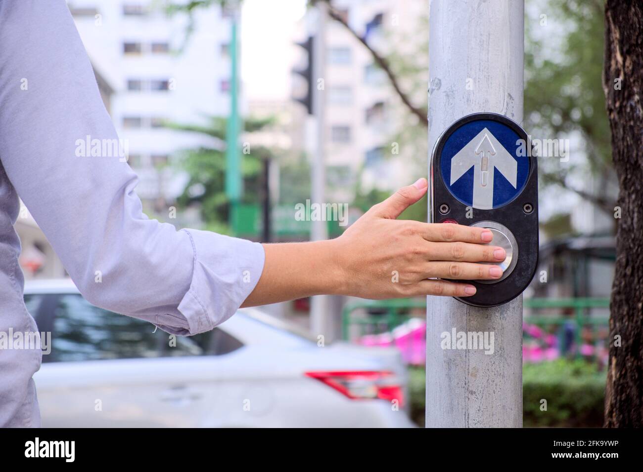 Back view and close-up hands of young businessman who push pedestrian crossing button and wait a green light signal for cross the road on metropolis Stock Photo