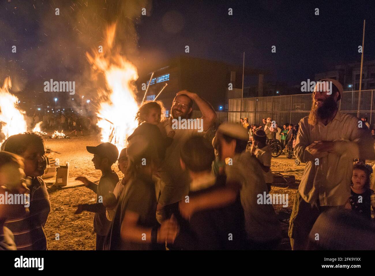 People dance near a fire during the Jewish Holiday of Lag Ba'Omer, which takes place every  18th of Hebrew month Iyar. It is customary during this holiday to make fires. This year, due to fire hazard warning, all fires were concentrated to few sites, hence the large number of pyres. Stock Photo