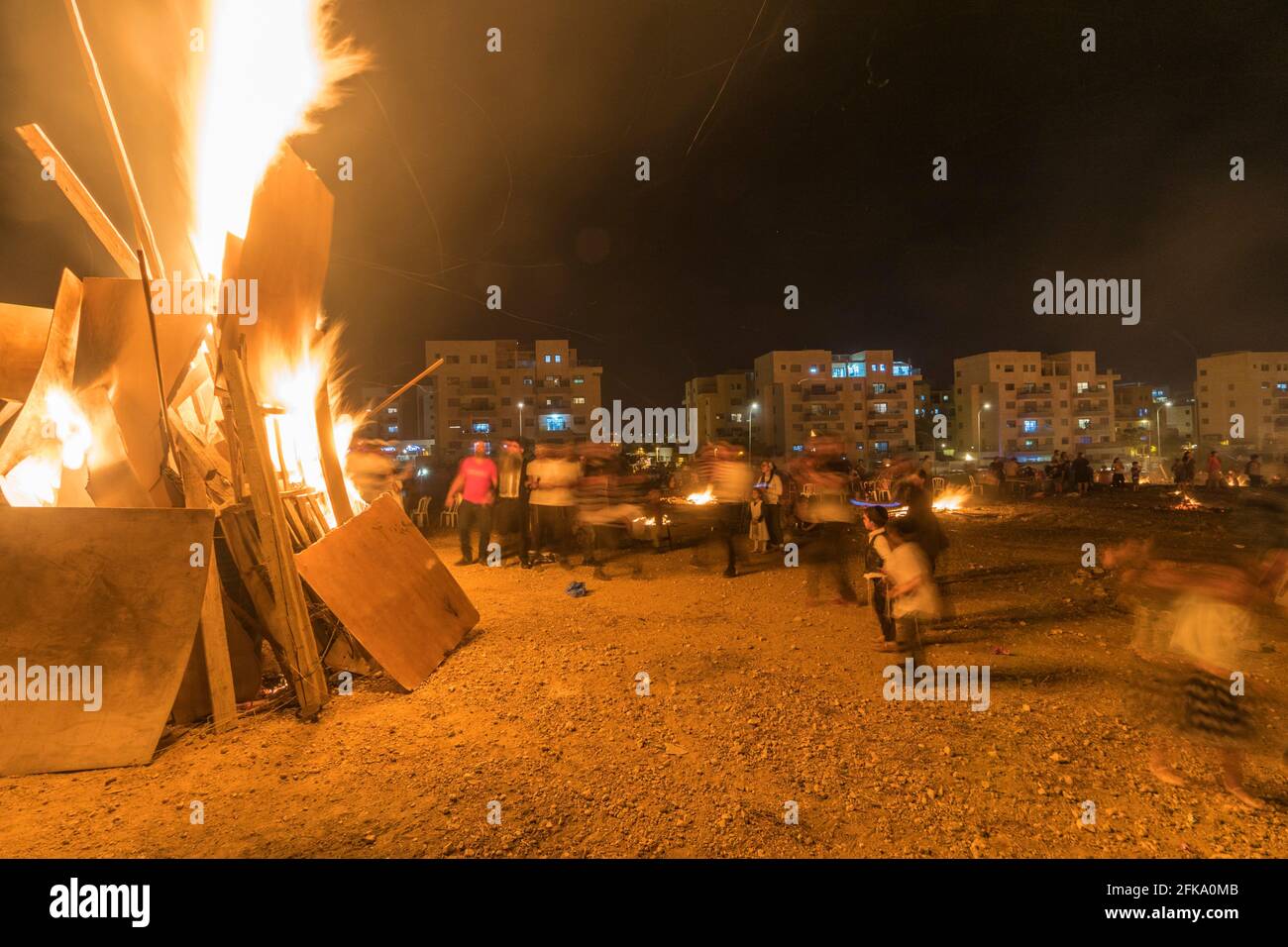 People dance around a fire during the Jewish Holiday of Lag Ba'Omer, which takes place every  18th of Hebrew month Iyar. It is customary during this holiday to make fires. This year, due to fire hazard warning, all fires were concentrated to few sites, hence the large number of pyres. Stock Photo