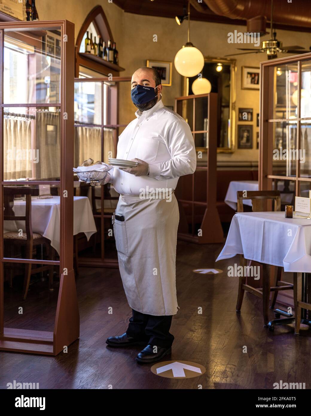 A waiter wears a mask and gloves while serving tables inside of a restaurant dining room during Covid Stock Photo