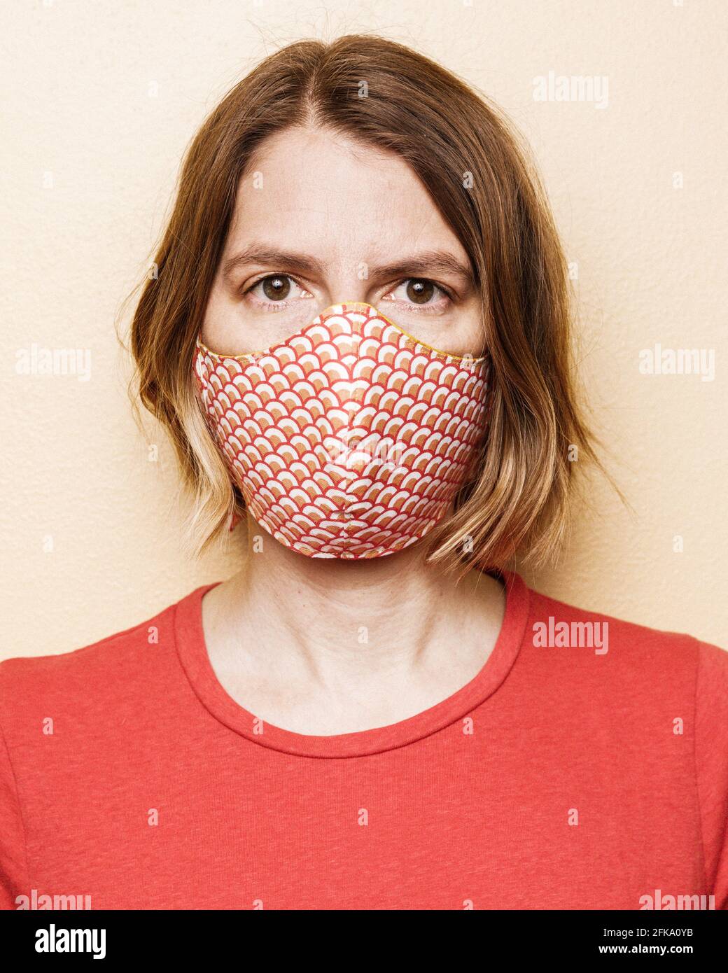 portrait of a woman with a red shirt and chin length hair wearing a hand sewn mask to cover her nose and mouth from COVID. Stock Photo