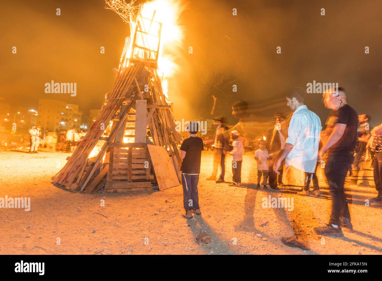 People near a large pyre during the Jewish Holiday of Lag Ba'Omer, which takes place every  18th of Hebrew month Iyar. It is customary during this holiday to make fires. This year, due to fire hazard warning, all fires were concentrated to few sites, hence the large number of pyres. Stock Photo