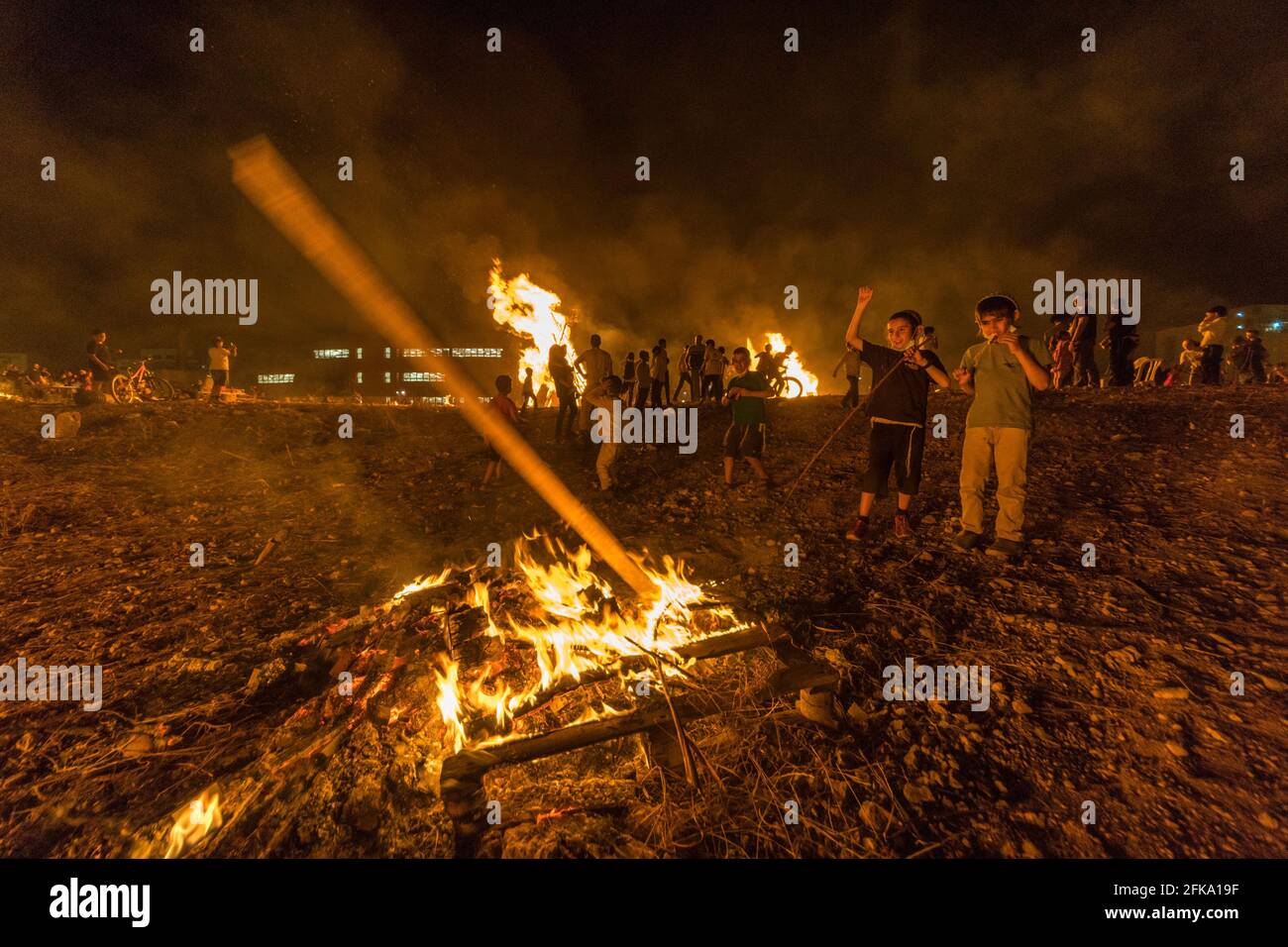 Children throw wood into a fire during the Jewish Holiday of Lag Ba'Omer, which takes place every  18th of Hebrew month Iyar. It is customary during this holiday to make fires. This year, due to fire hazard warning, all fires were concentrated to few sites, hence the large number of pyres. Stock Photo