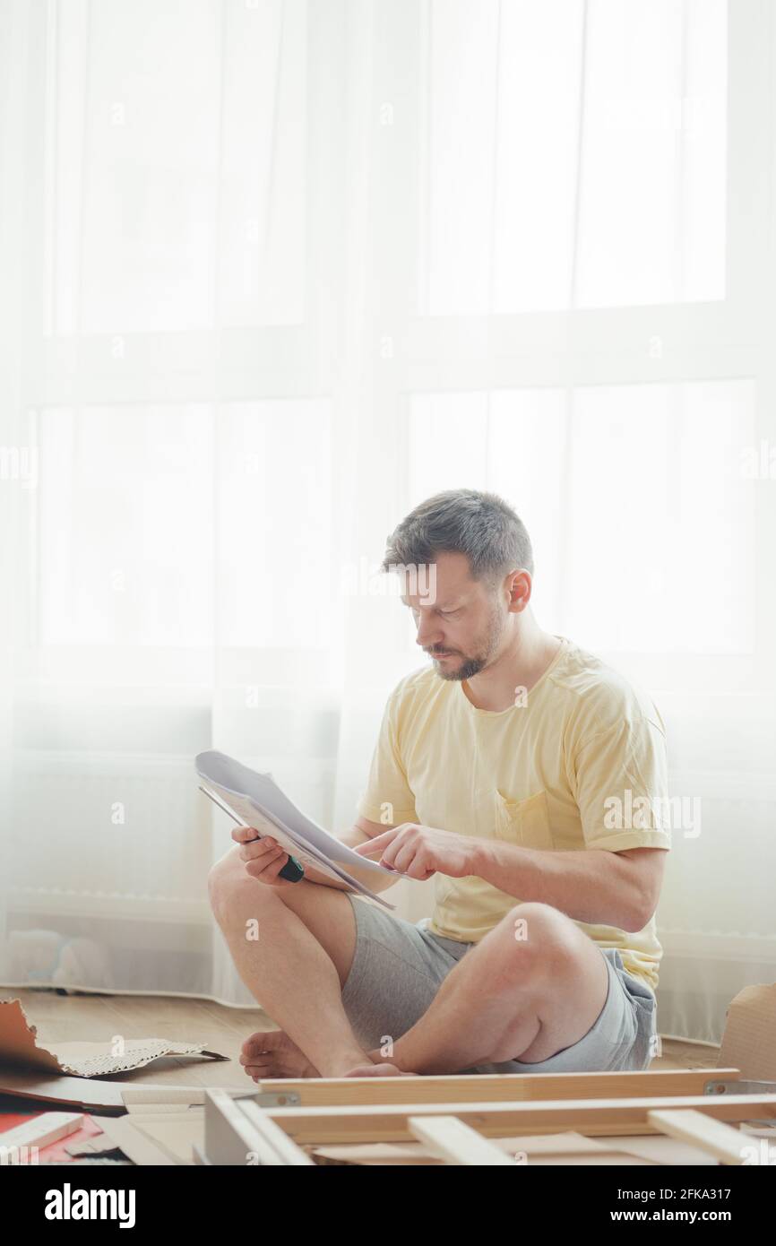 Young attractive man in a yellow T-shirt assembles furniture Stock Photo