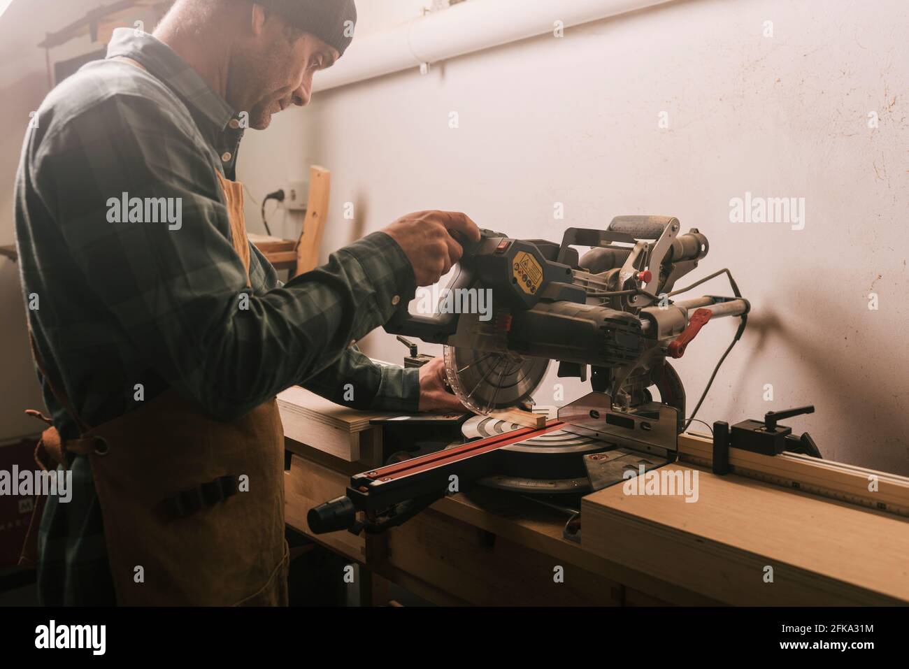 Side shot of a cabinetmaker cutting a wood strip with a circular saw. Stock Photo