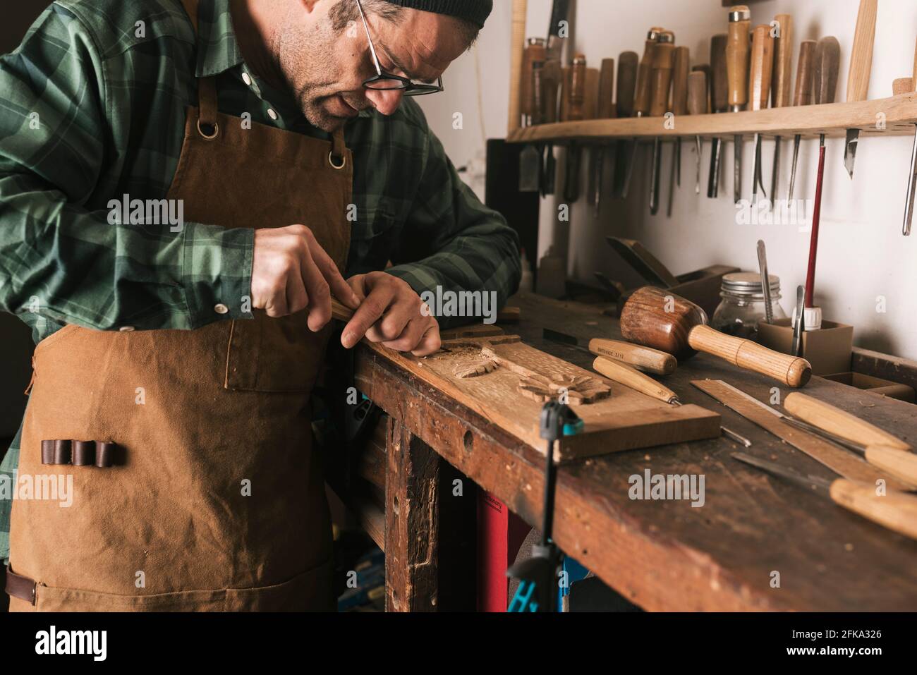 Side shot of a cabinetmaker working on a wood carving with a chisel. Stock Photo