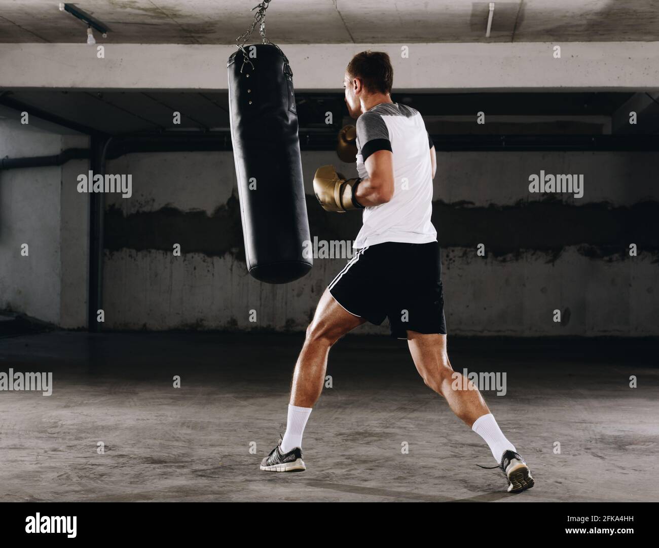 Young muscle boxer using a punching bag in gym. Boxer hitting punching