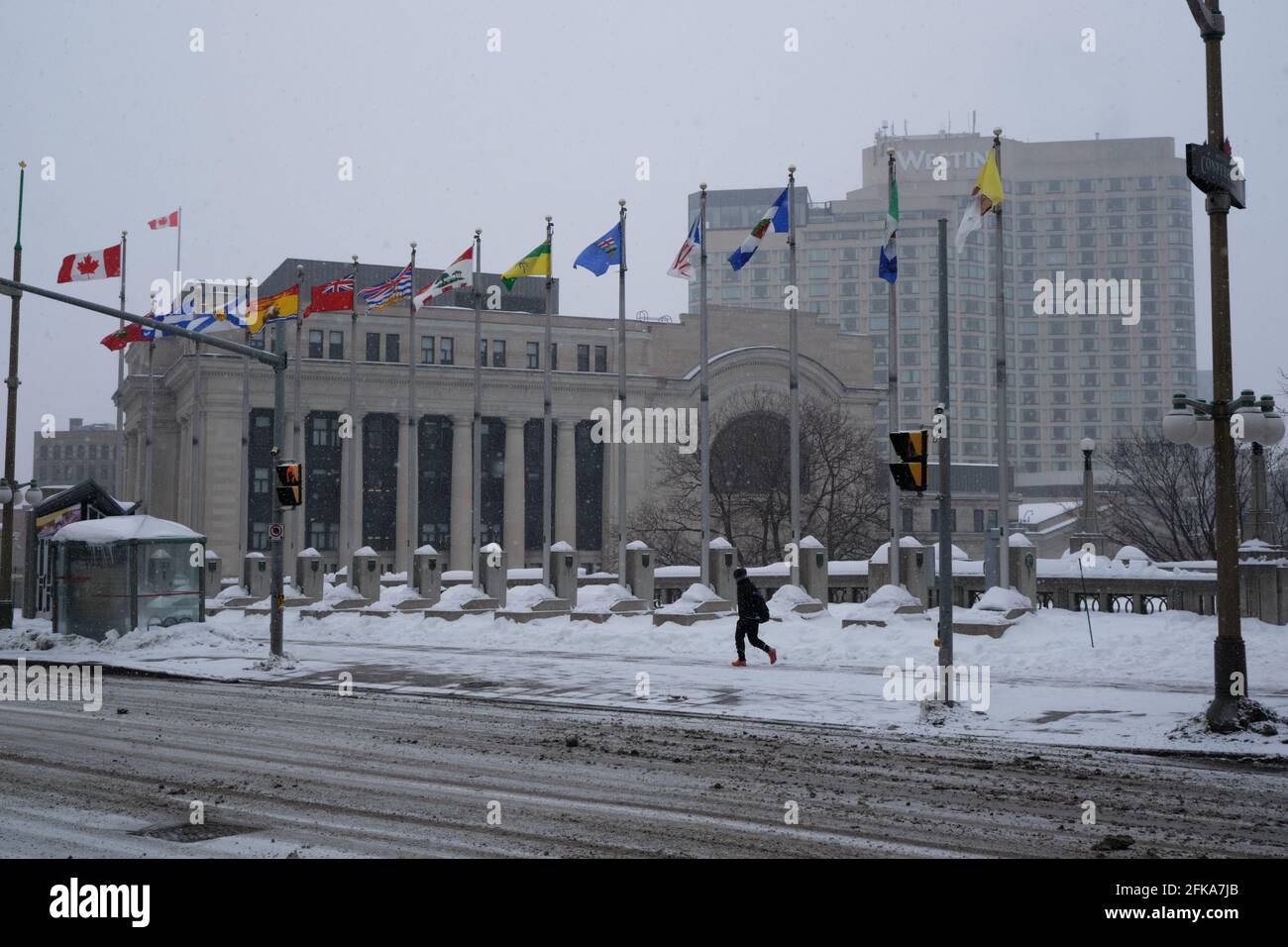 Centre of Ottawa on snowy storm winter day, with the old Train station and the Westin hotel in background while pedestrian walks on sidewalk Stock Photo