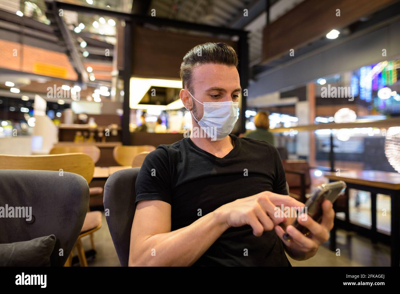 Man sitting at coffee shop while social distancing and using mobile phone and wearing face mask Stock Photo