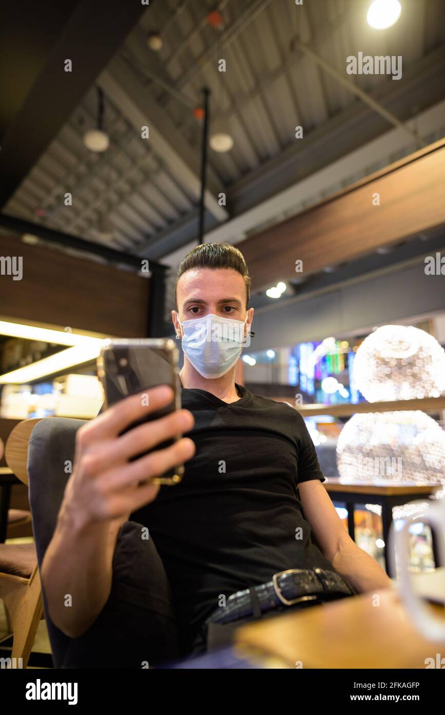 Man sitting at coffee shop while social distancing and using mobile phone and wearing face mask Stock Photo