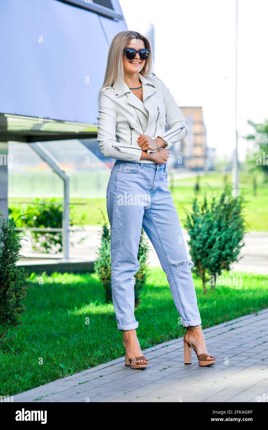 Pretty lady in blue jeans and white leather jacket enjoying sun Stock Photo