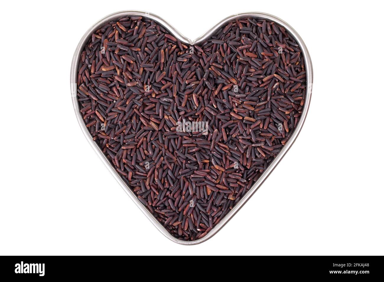 Heart shaped tin pan full of raw Riceberry rice grains in reddish purple shade grown in Thailand, isolated on white background. It is a crossbred betw Stock Photo
