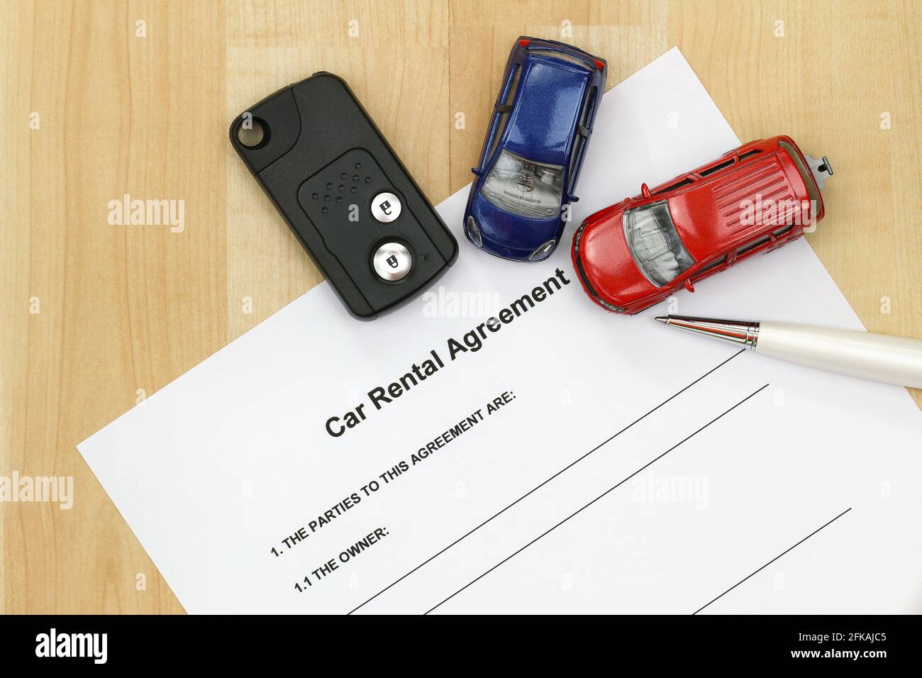 Closeup of car rental agreement paper next to a remote car key, a pen and mini car models Stock Photo