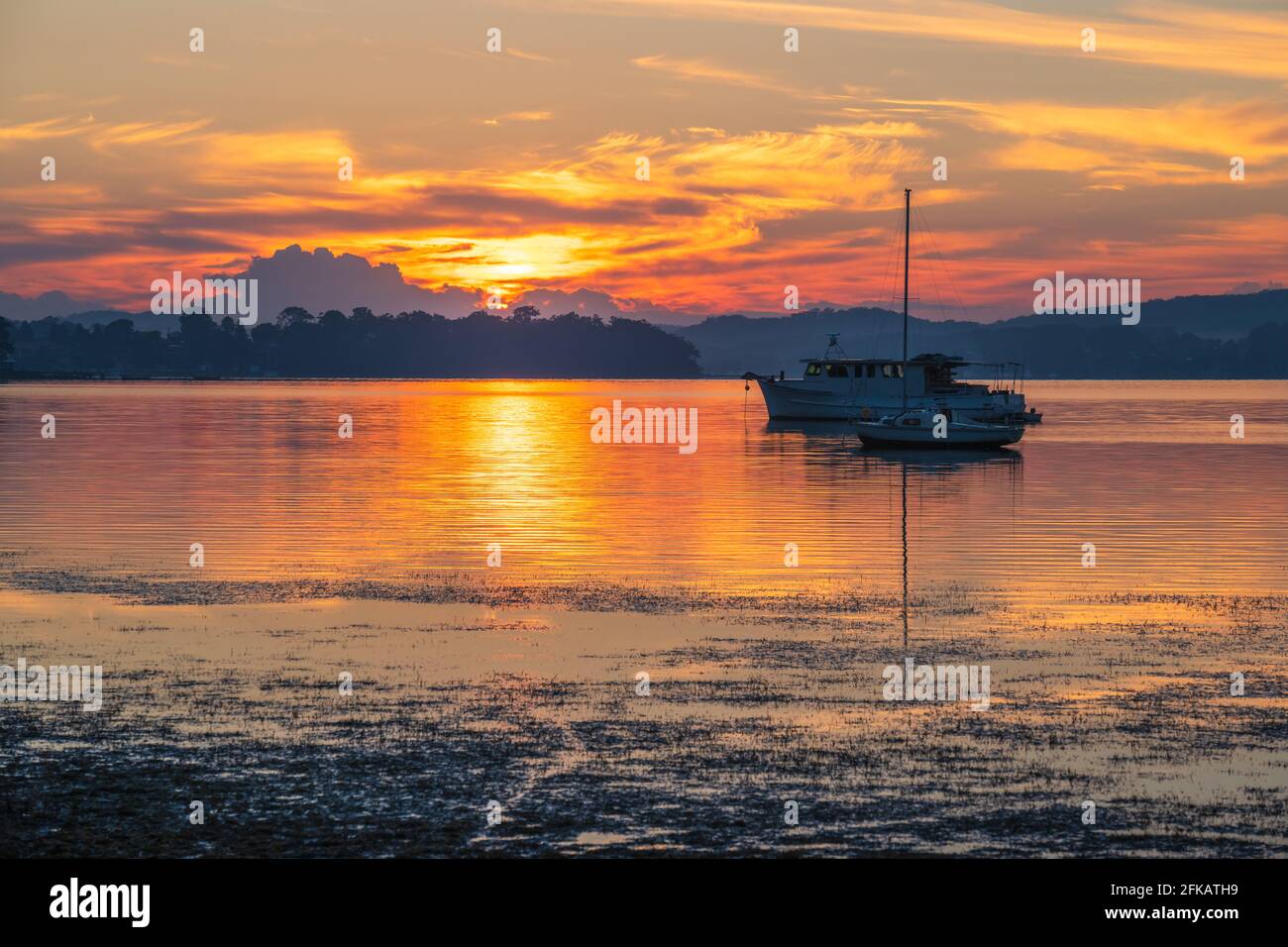 A pretty sunrise with boats and reflections at Koolewong Waterfront on the Central Coast, NSW, Australia. Stock Photo