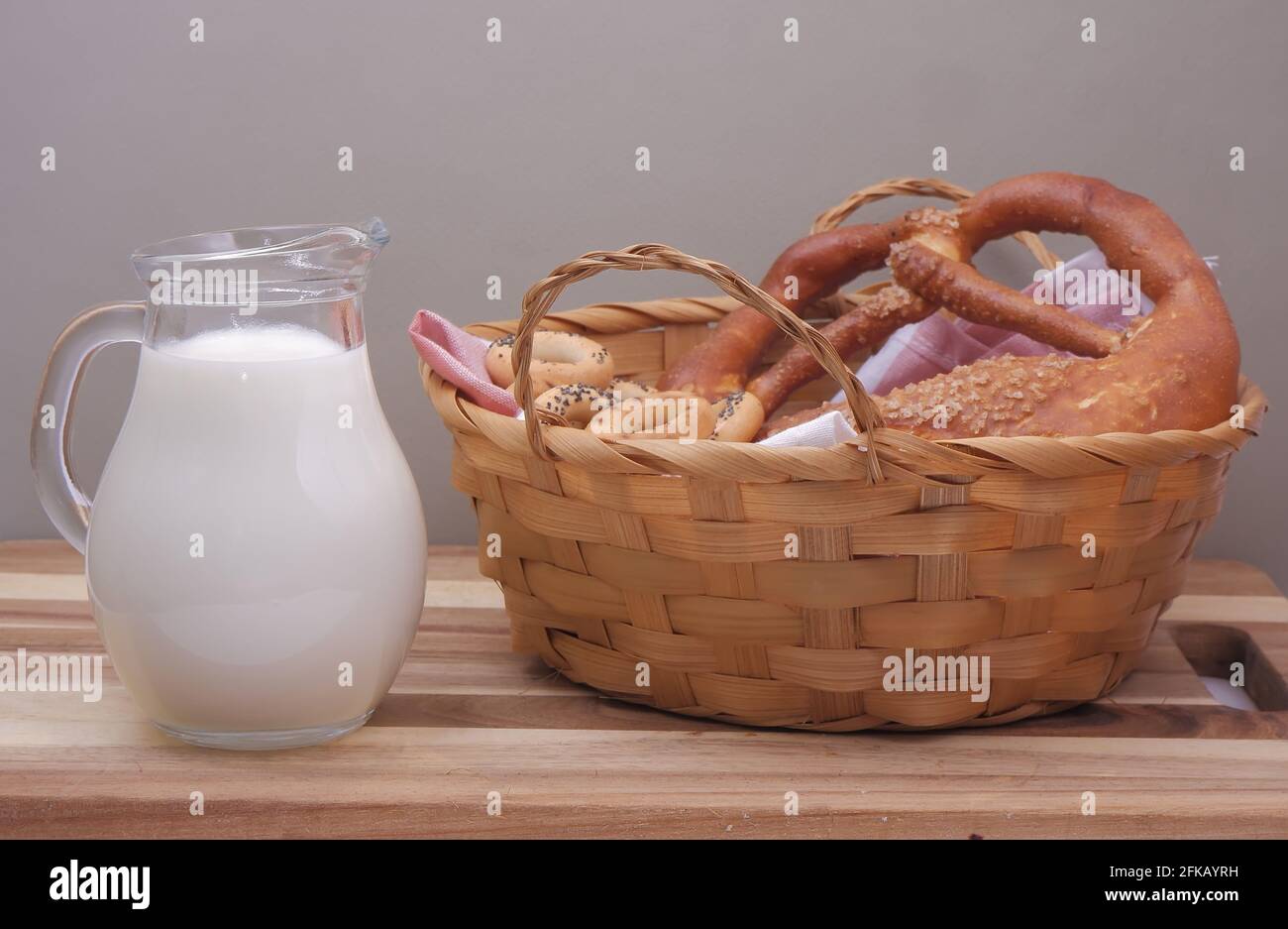a glass jug of milk sits on the cutting board next to a basket of buns and dried poppy seeds. Stock Photo