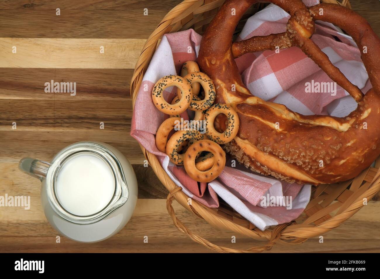 a glass jug of milk sits on the cutting board next to a basket of buns and dried poppy seeds. Stock Photo