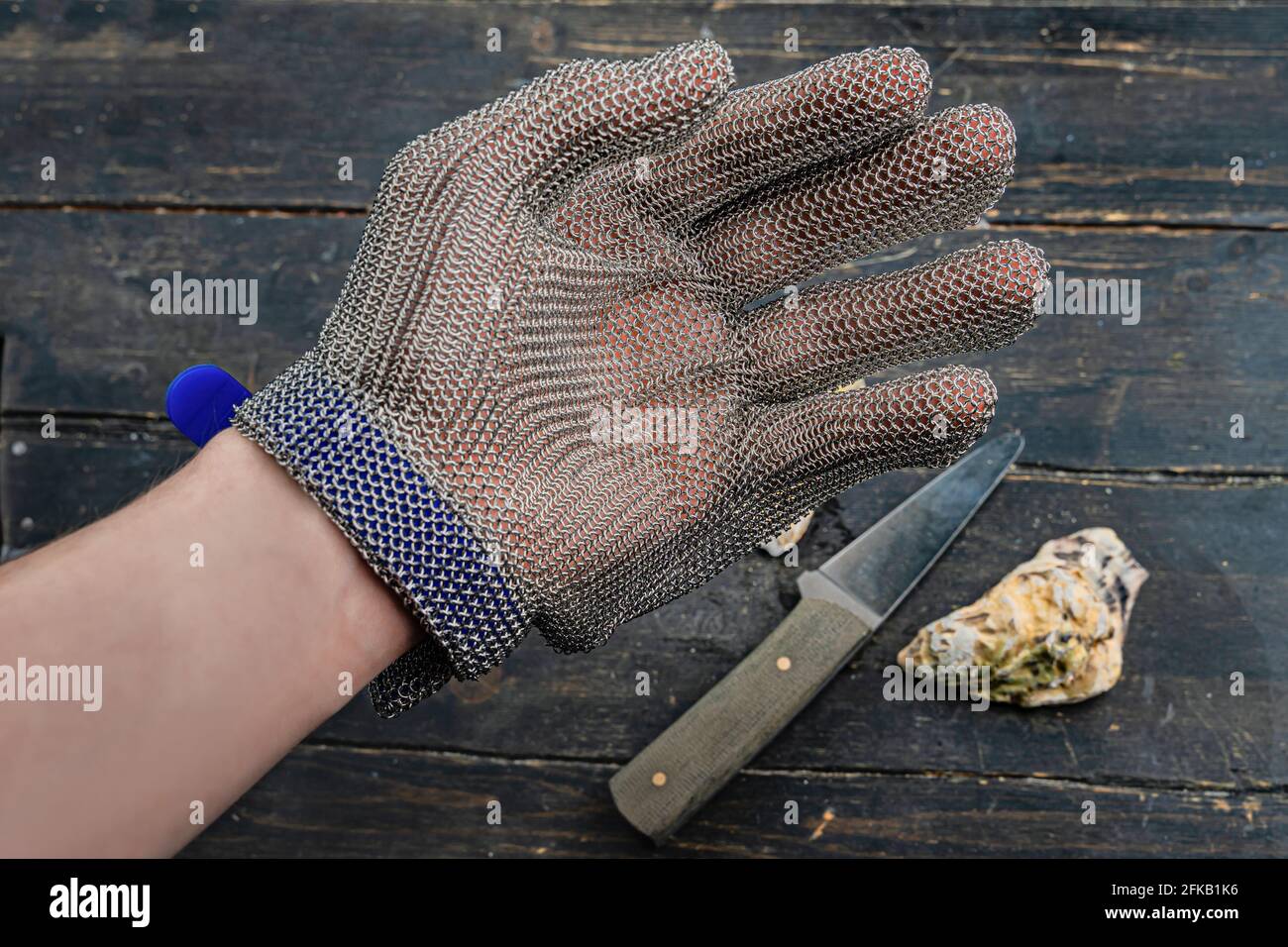 Hand in protective gloves. Close up. Oyster and knife in the background Stock Photo