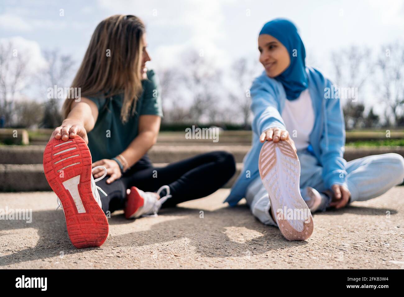 Multicultural female friends sitting in the park stretching their legs ...