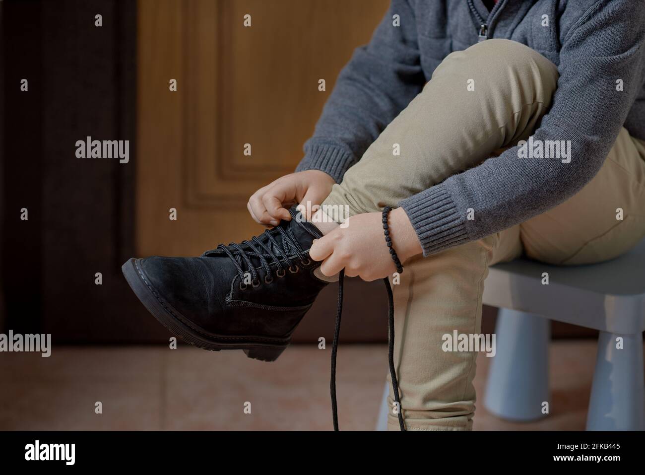 Child learning to tie shoelaces on boots before leaving home, selective focus Stock Photo