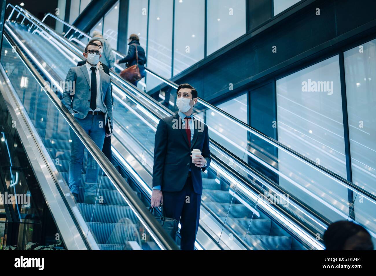 Business people moving down on escalator during pandemic Stock Photo