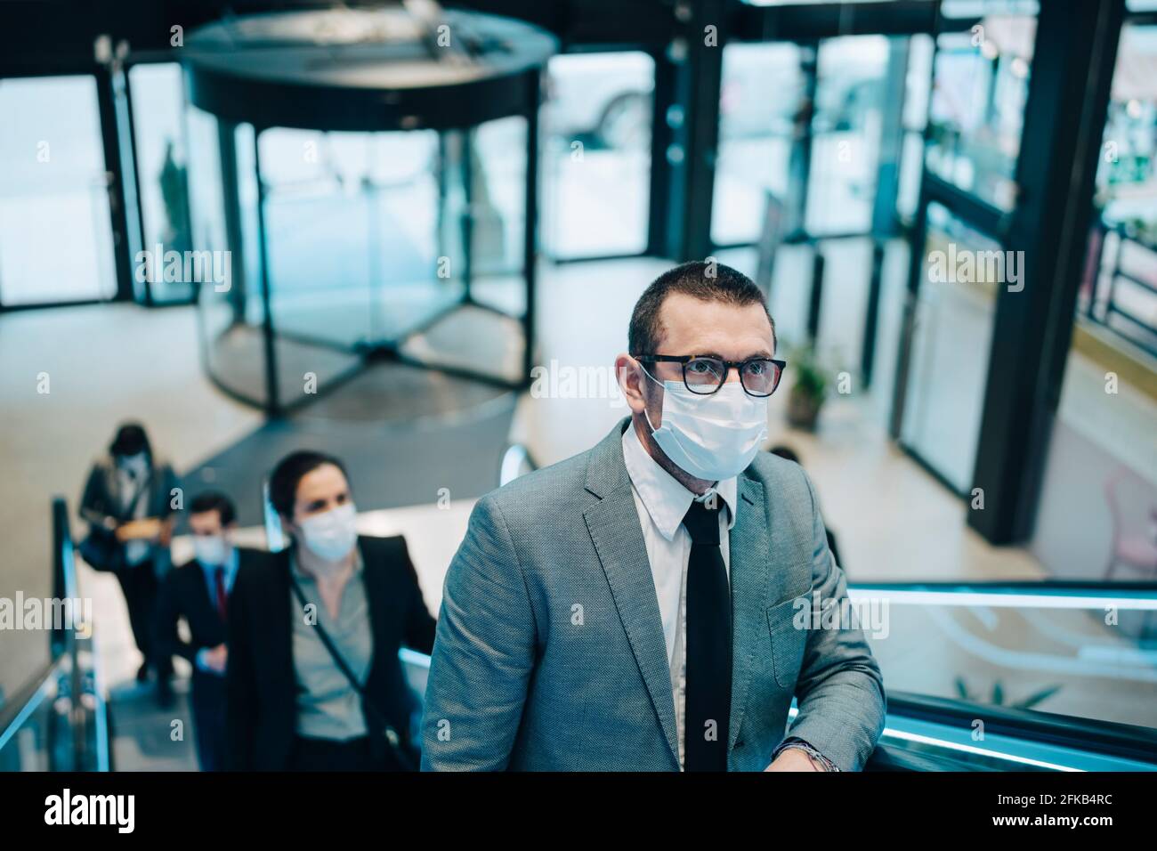 Business people moving upwards on escalator during pandemic Stock Photo