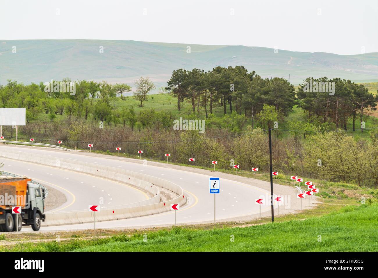 An empty highway with a sharp turn through green forest and hills Stock Photo
