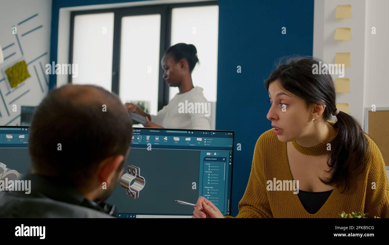 Mechanical engineers using computer, discussing about manufacturing new project, taking notes on clipboard. Man technician working at pc, screen shows 3D engine made with CAD software. Stock Photo