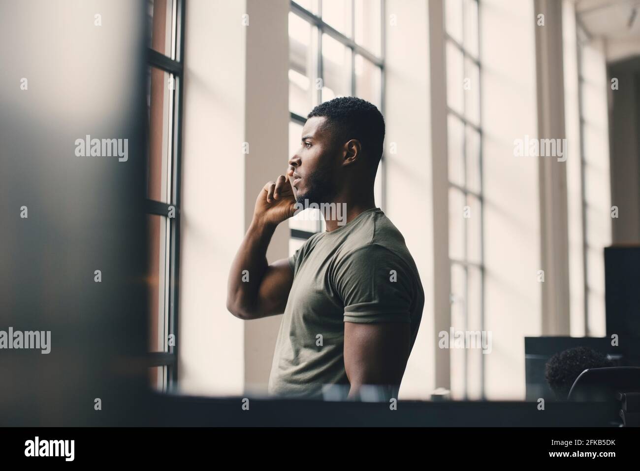 Male entrepreneur talking on mobile phone while looking through window in office Stock Photo