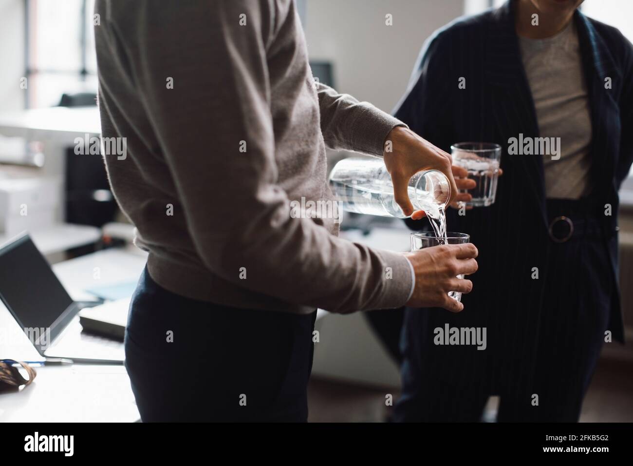 Midsection of businessman pouring water in drinking glass in office Stock Photo